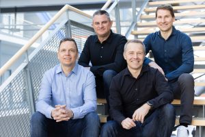 Vier lächelnde Gründer von BOXID sitzen in Business-Kleidung auf einer Innentreppe.