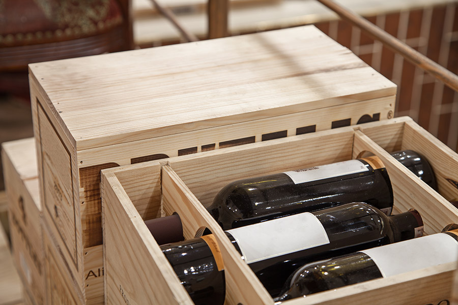 Holzkiste mit mehreren Flaschen wertvollen Weins, teils offen zum Einblick, auf elegantem Hintergrund.